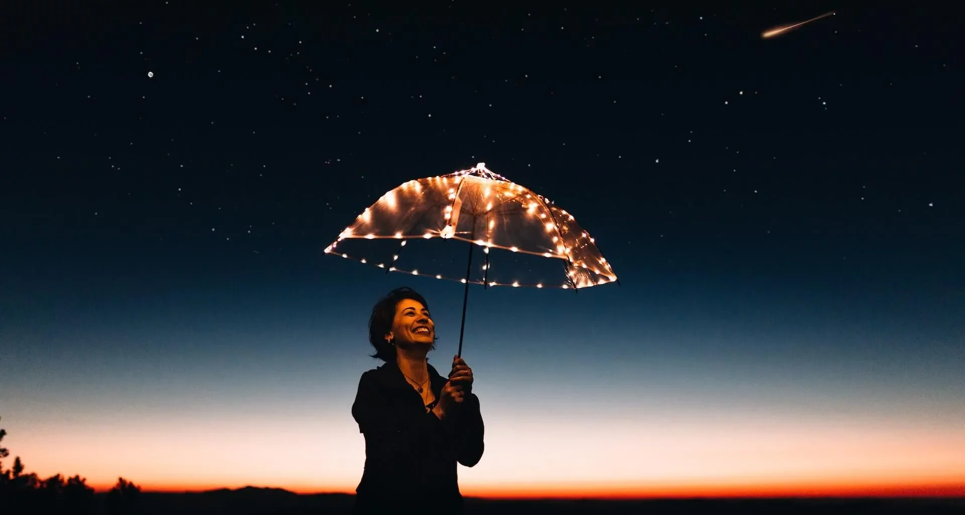 A woman is looking at the umbrella which is illuminated